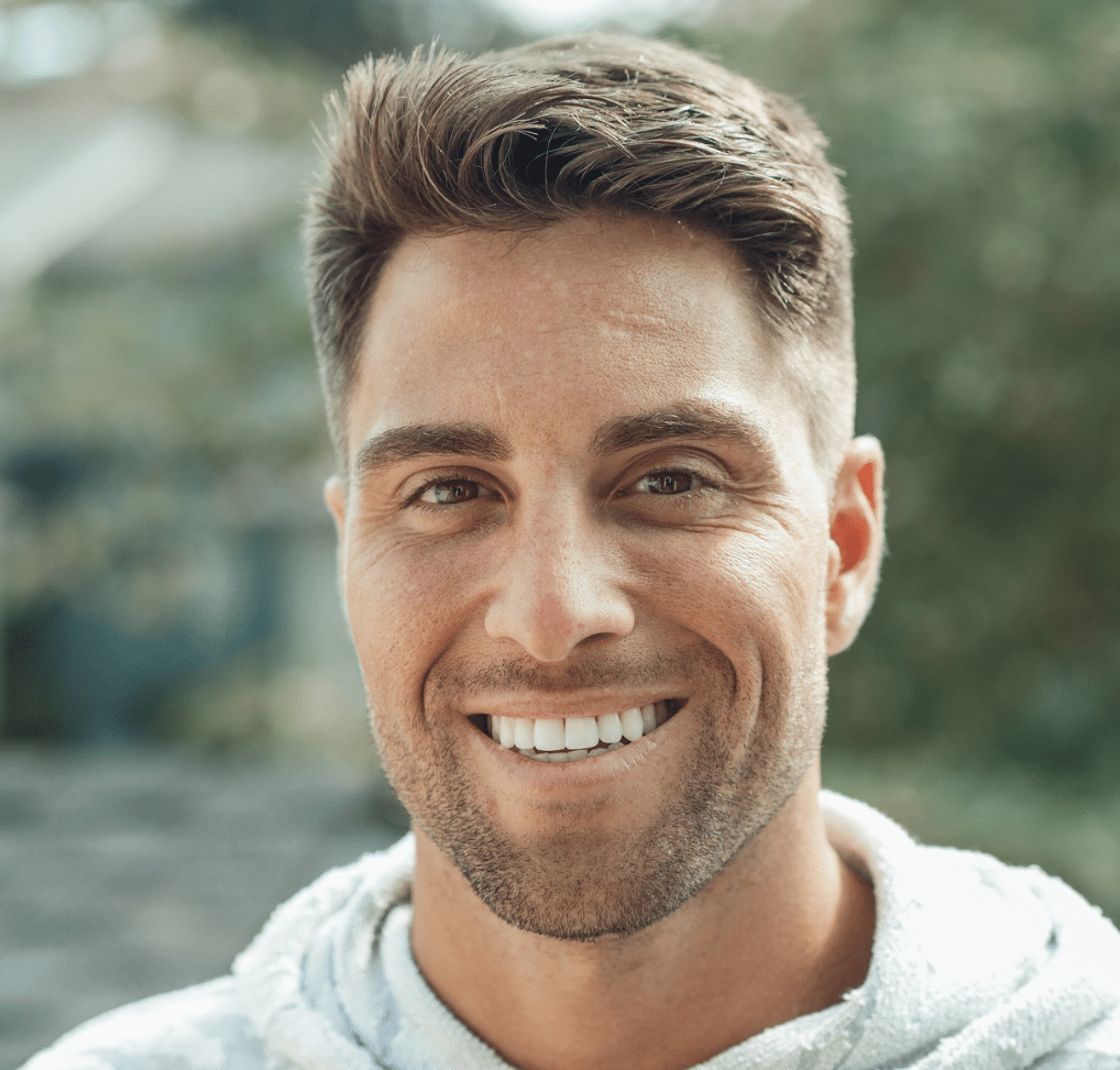 A young man with short brown hair and trimmed facial hair is smiling outdoors. He is wearing a light-coloured hoodie, enjoying nature whilst practising smart screen time management with ScreenCoach.
